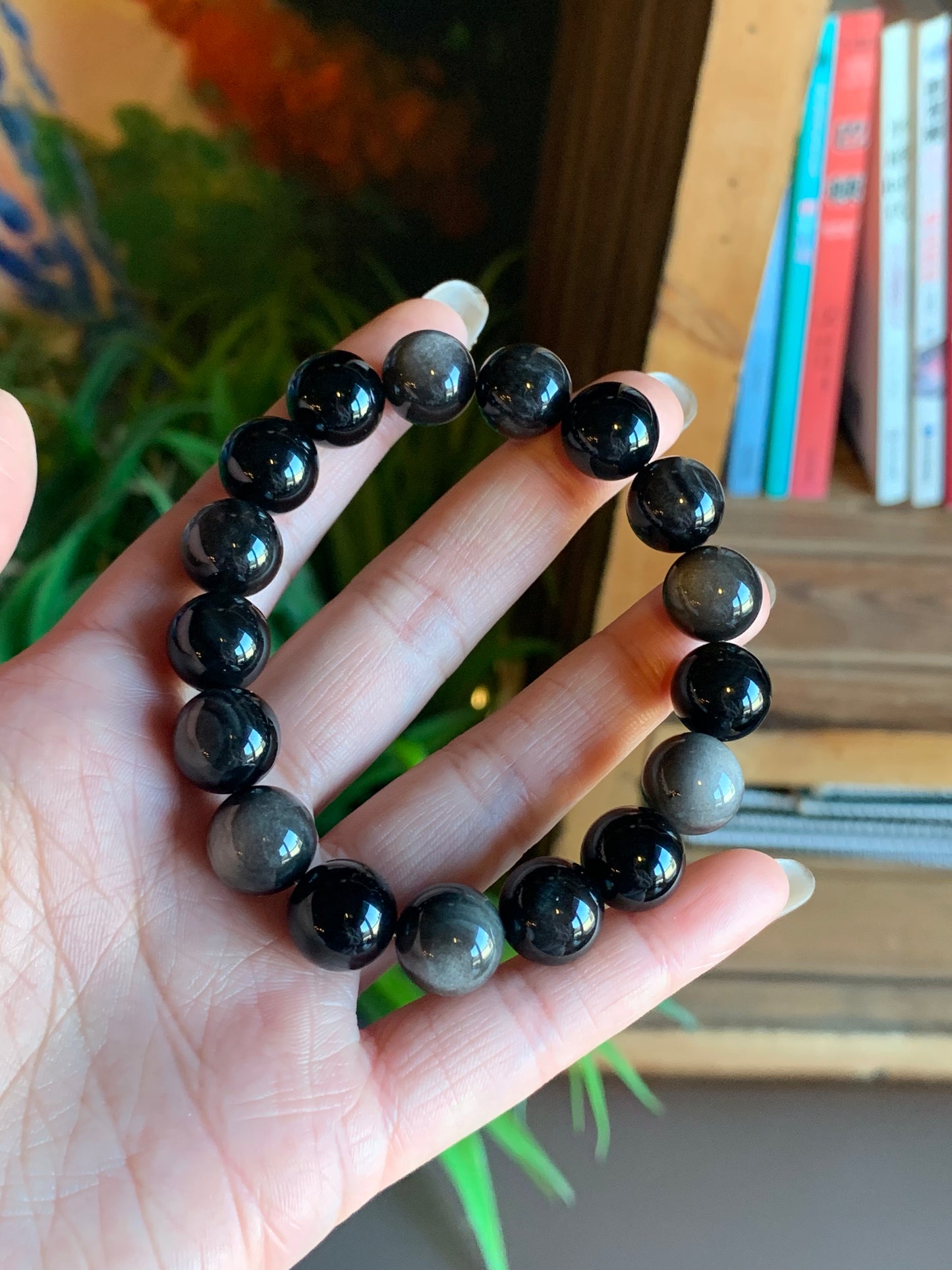 Close-up hand-holding view of the Harmony Power 12mm Obsidian Bracelet within a natural and academic surroundings, showcasing the intricate details of the obsidian beads and their protective properties.