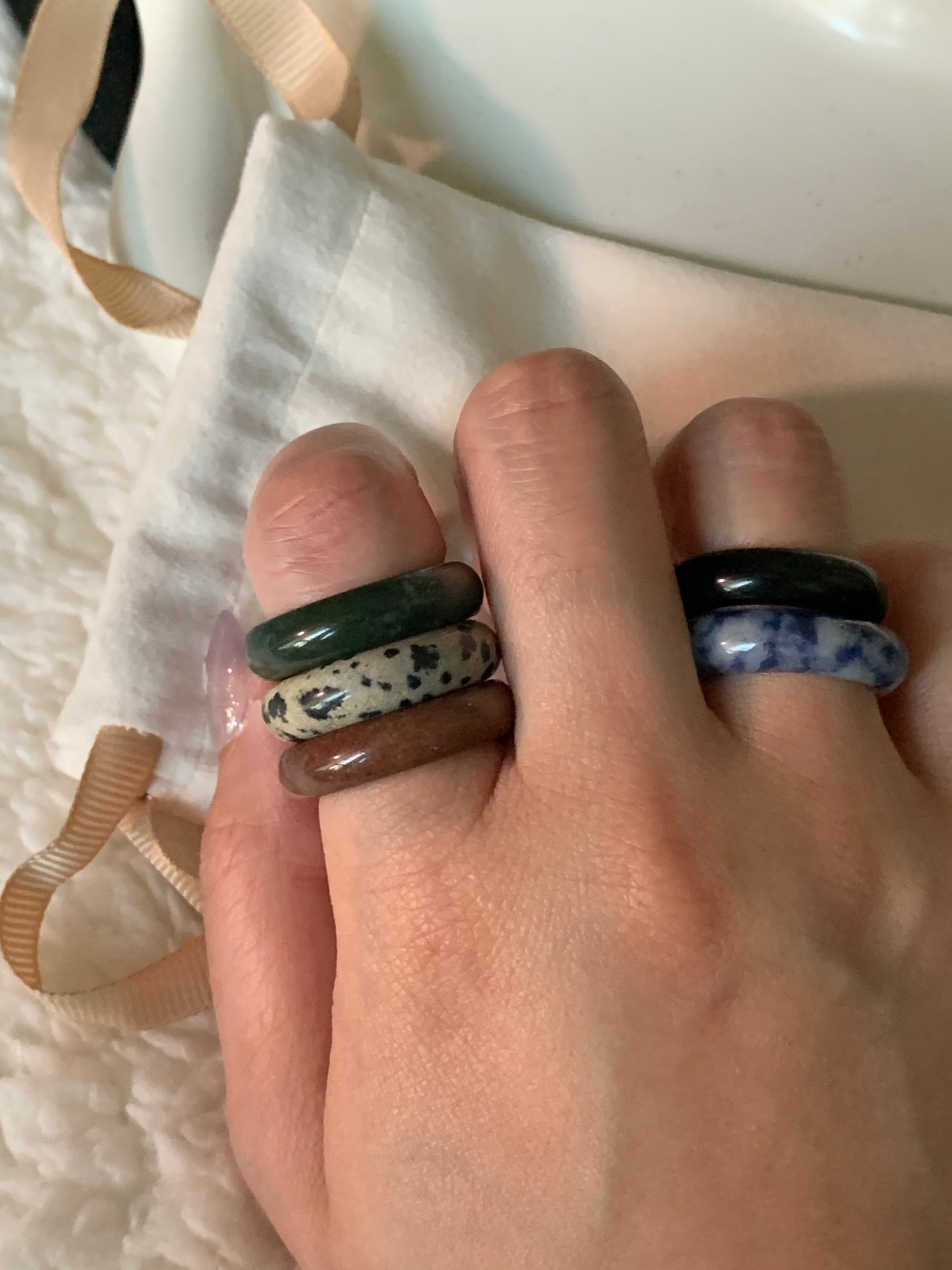 A close-up view of various rings stacked for a trendy layered look, featuring stones like Rose Quartz and Tiger's Eye.