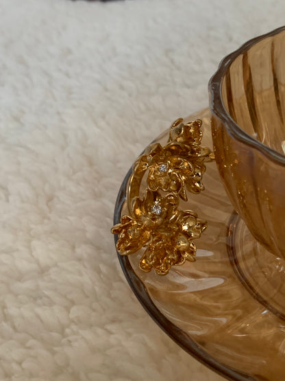 Gold Twins Flower Ring placed in a brown cup with plate on white blanket.